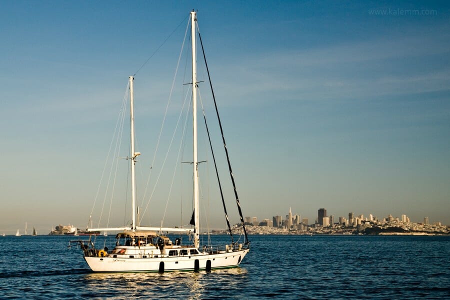 a sailboat drives across the San Francisco Bay, with the city’s skyline in the background