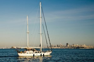 A sailboat sets sail in the evening light in front of the San Francisco skyline